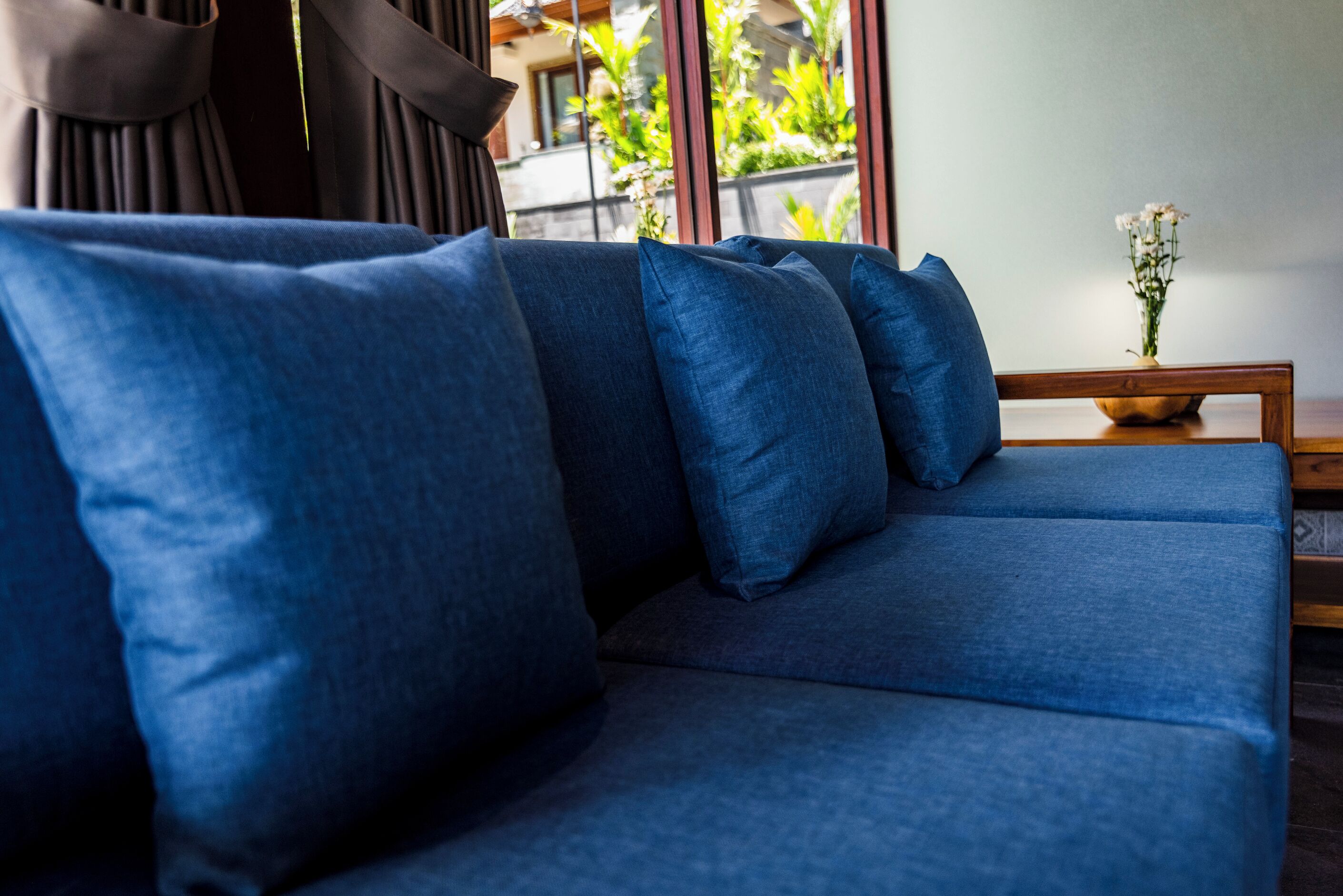Un salon moderne avec un canapé bleu et une table d’appoint en bois sur laquelle est posé un vase de fleurs.