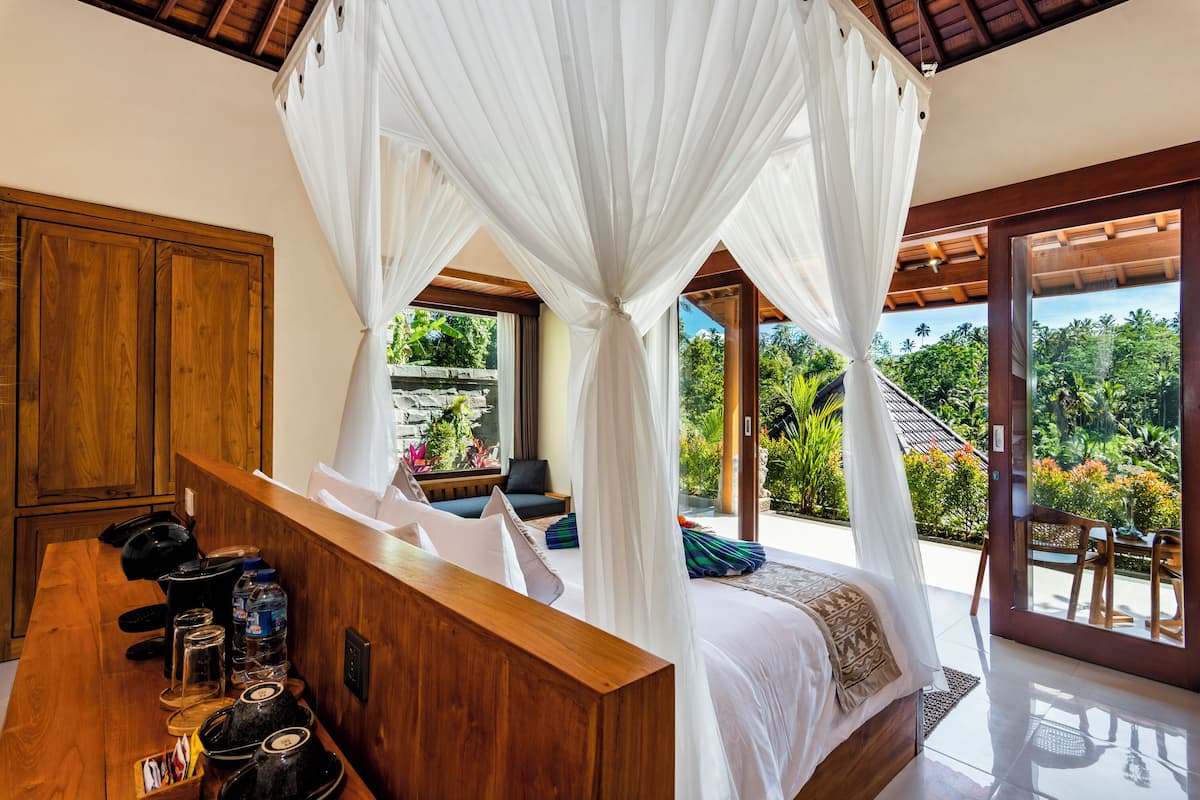 A bedroom with a canopy bed, wooden furniture, and a view of lush greenery.