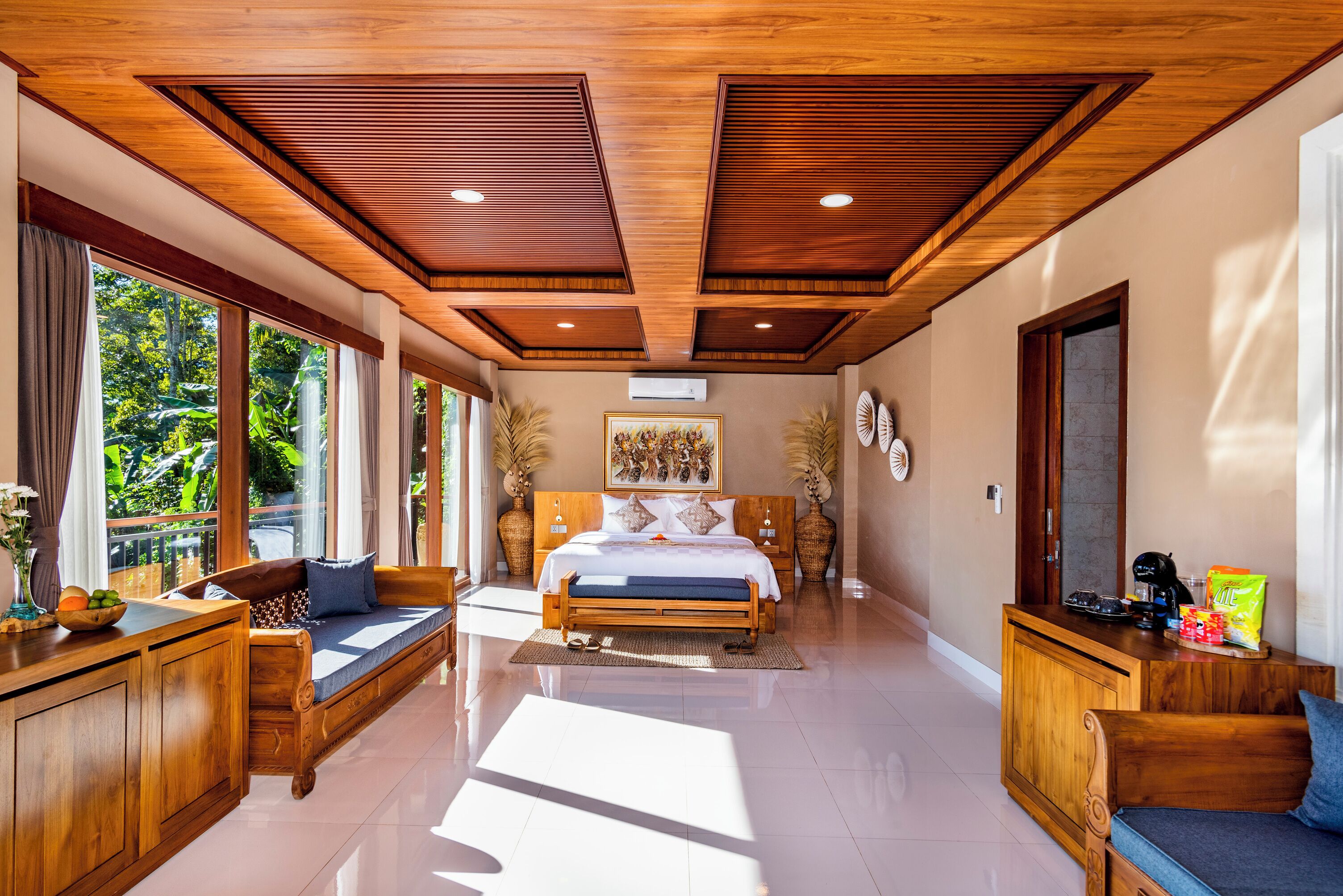 A spacious bedroom with a large bed, wooden ceiling, and a view of greenery outside.