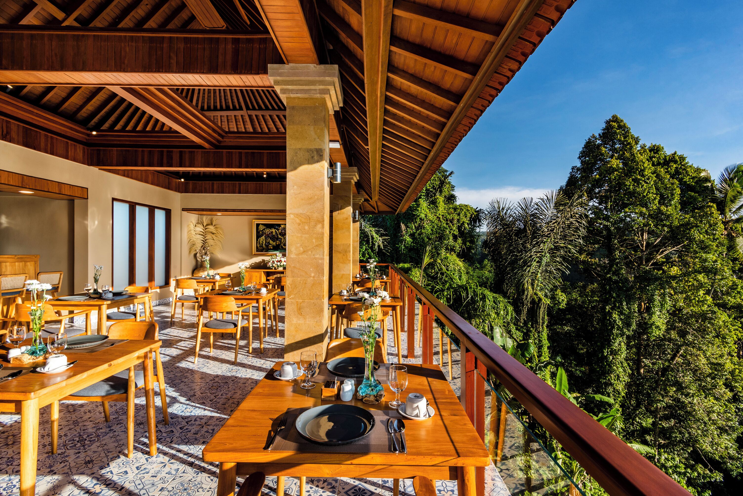 A restaurant with wooden tables and chairs, a tiled floor, and a view of lush greenery.