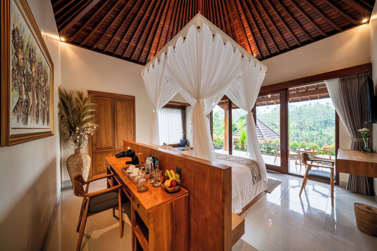 A bedroom with a canopy bed, wooden furniture, a dining area, and a view of the outdoors.