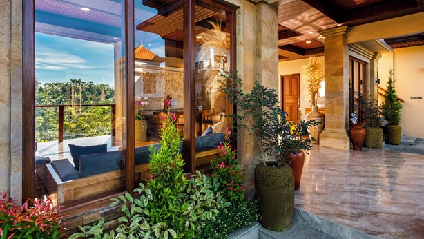 A spacious indoor area with large windows, a wooden bench, and potted plants. - Ellena Hilltop Resort Ubud by Dhananjaya Hospitality (Sebatu)