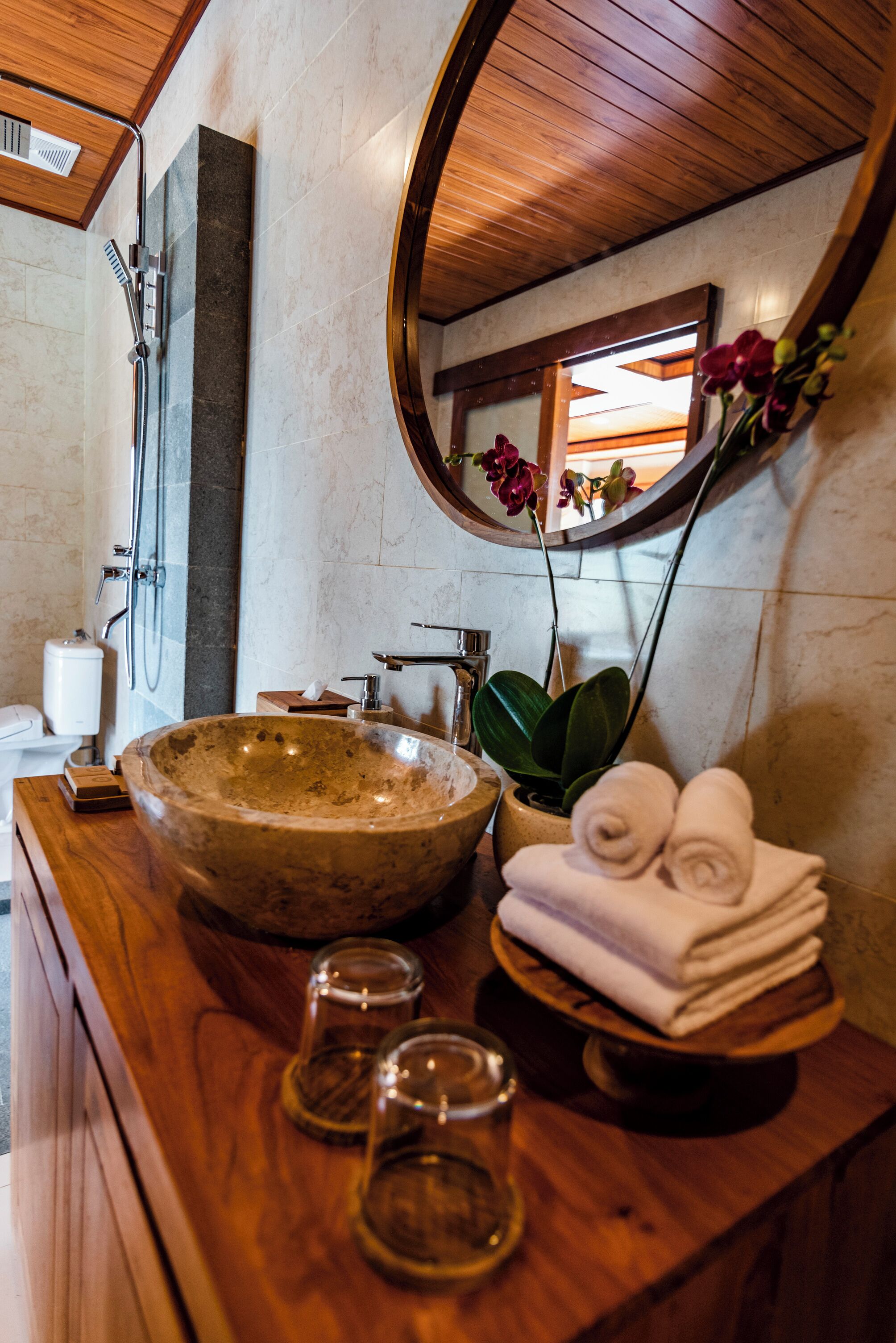 Une salle de bain avec un meuble-lavabo en bois, un grand lavabo en pierre, un miroir et une plante en pot.