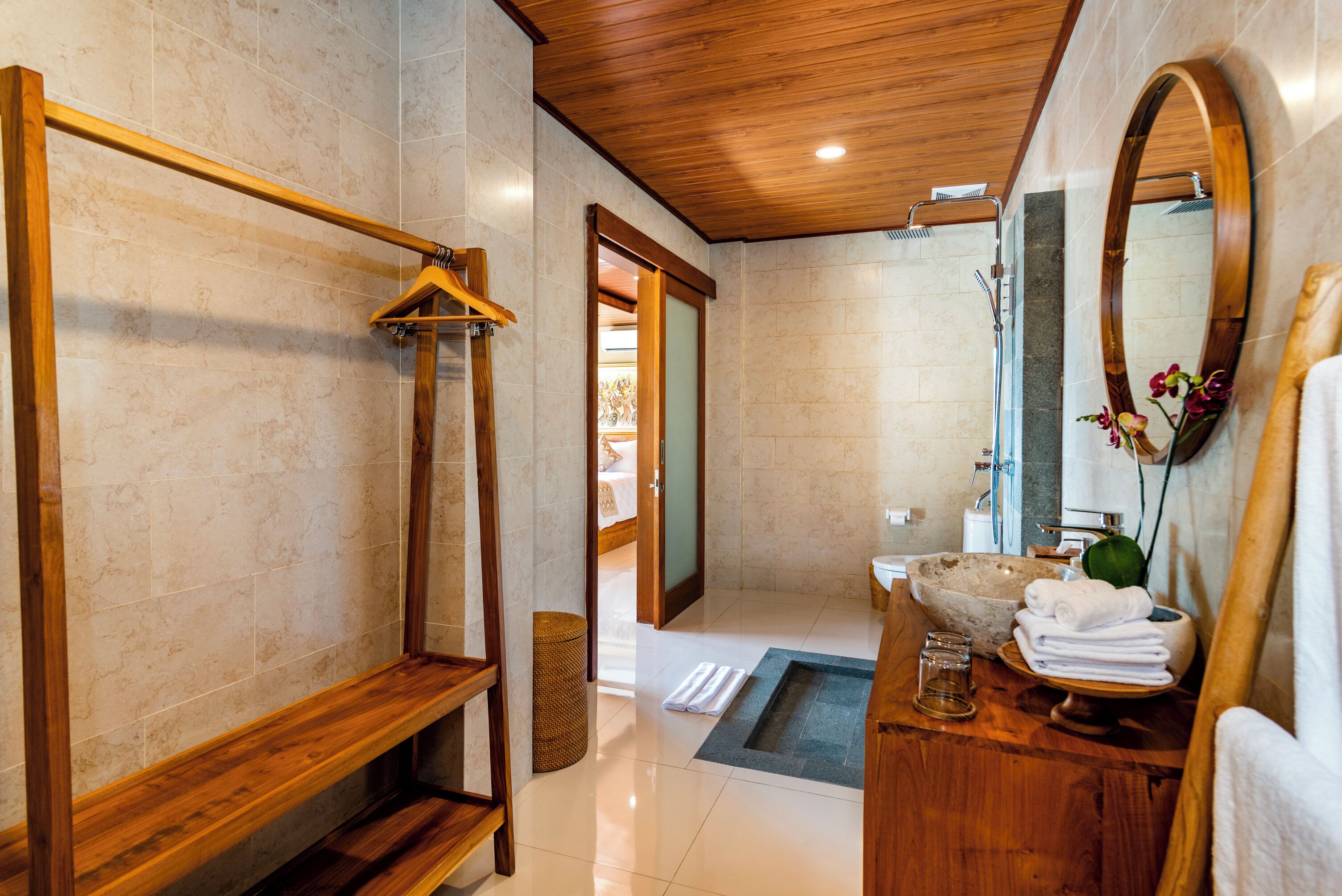A modern bathroom with a wooden vanity, a large mirror, a stone sink, and a walk-in shower.
