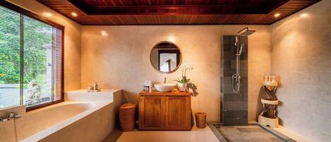 A modern bathroom with a wooden ceiling, a large bathtub, a round mirror, a sink with a wooden vanity, and a shower area.