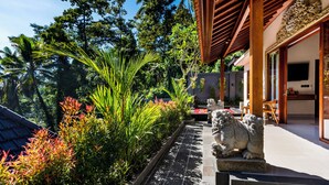 A traditional Balinese house with a tiled pathway, lush greenery, and stone lion statues. - Ellena Hilltop Resort Ubud by Dhananjaya Hospitality (Sebatu)