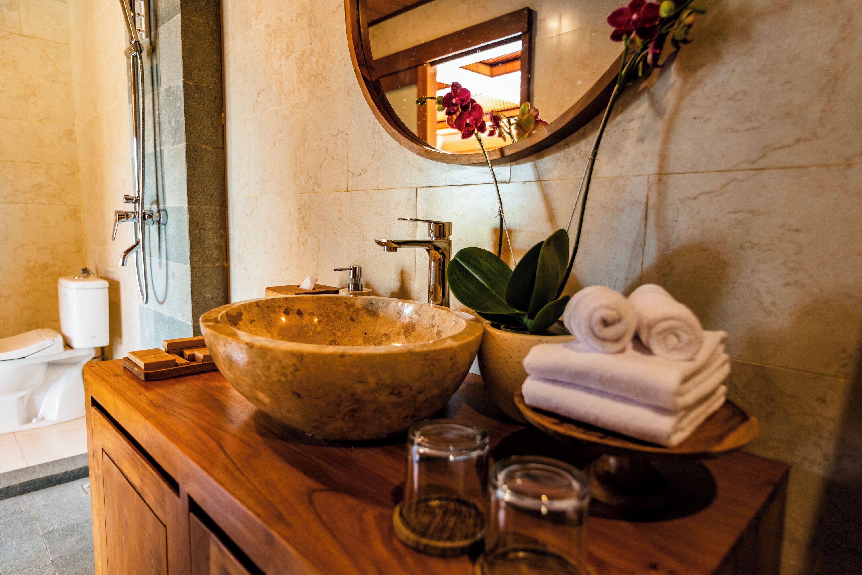 A bathroom with a wooden vanity, a large bowl sink, a mirror, and a stack of towels.