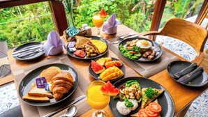 A breakfast table with plates of food, utensils, and a glass of orange juice. - Ellena Hilltop Resort Ubud by Dhananjaya Hospitality (Sebatu)