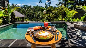 A breakfast setting with a poolside view, including a plate of eggs, toast, and a drink, surrounded by lush greenery. - Ellena Hilltop Resort Ubud by Dhananjaya Hospitality (Sebatu)