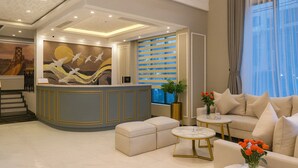 Een moderne lobby met een receptiebalie, een groot abstract kunstwerk, een trap en een zithoek met uitzicht op de stad.