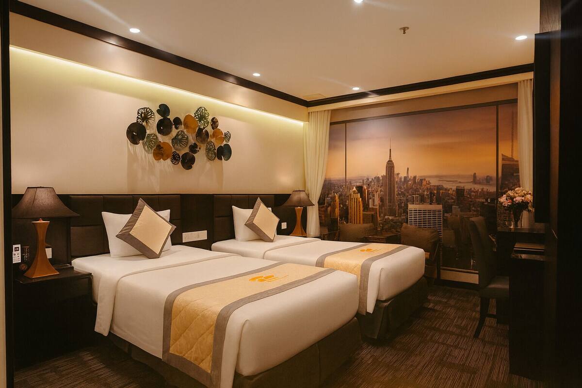 Habitación de hotel con dos camas, vistas a la ciudad, un adorno en la pared y un escritorio con lámpara.