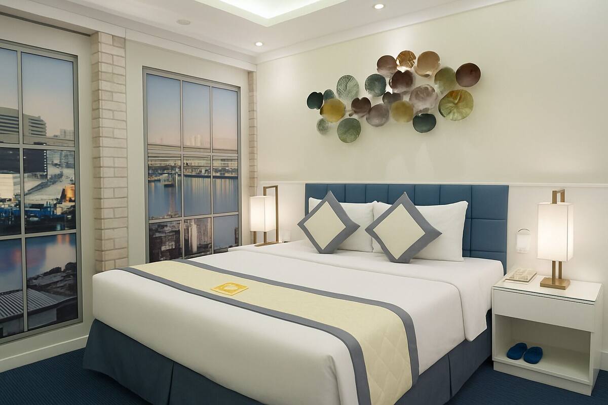 Una habitación de hotel con una cama grande, dos mesitas de noche, vistas a la ciudad a través de ventanales del suelo al techo y una obra de arte decorativa en la pared.