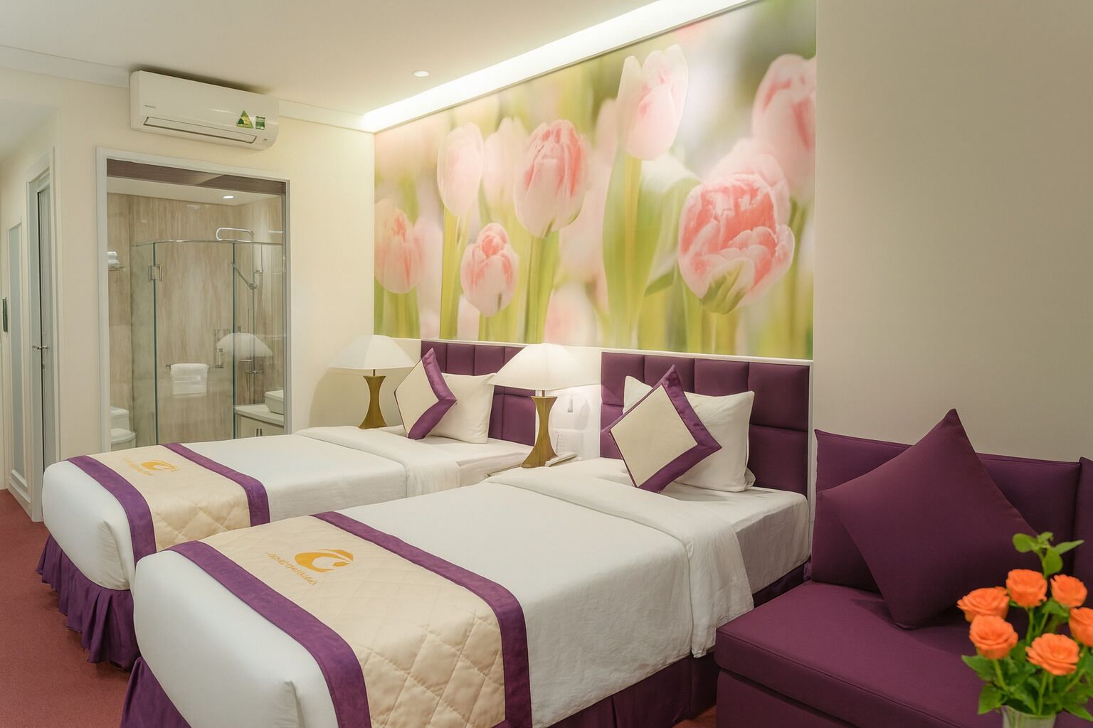 A hotel room with two beds, a shower area, and a purple sofa.