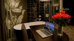 Een moderne badkamer met een grote spiegel, een douche en een zithoek met een laptop en rozen.