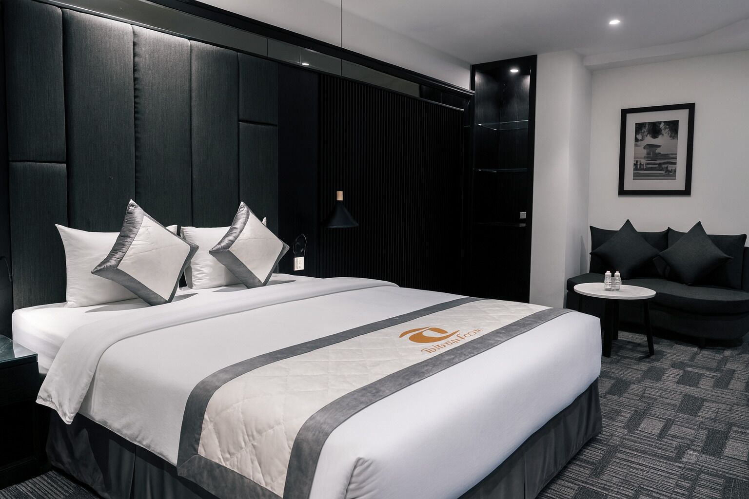 Ein modernes Hotelzimmer mit einem großen Bett, einer kleinen Couch, einem Beistelltisch und einem gerahmten Bild an der Wand.