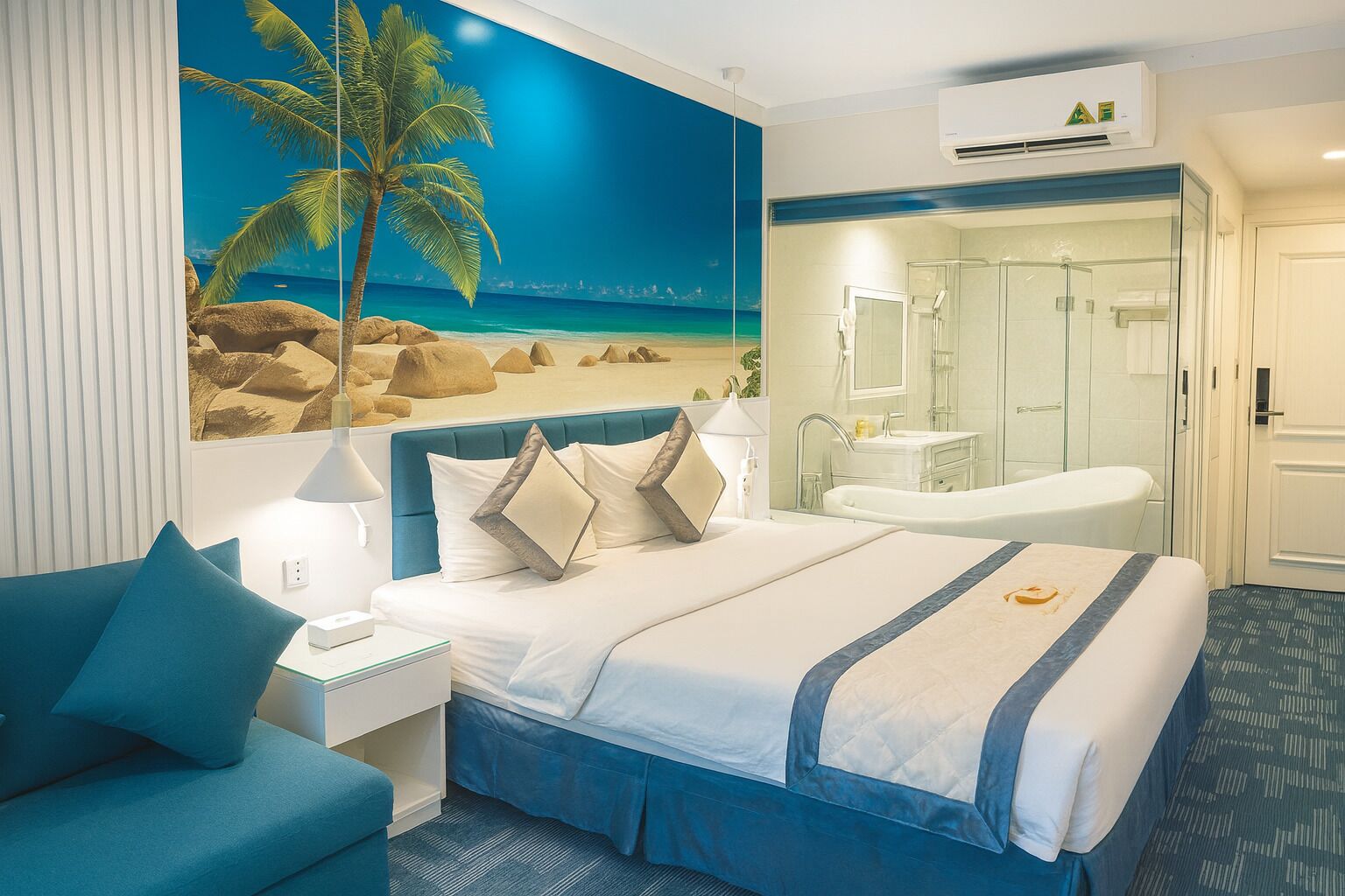 A hotel room with a bed, a nightstand, a desk, a bathroom with a shower, and a large beach mural on the wall.