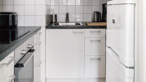 A modern kitchen with white cabinets, a black countertop, a stainless steel sink, a kettle, and a white refrigerator. - Bright Studio Apt. with Private Balcony  (Helsinki)