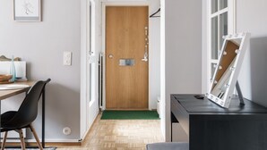A room with a wooden door, a mirror with lights, a desk with a chair, and a patterned rug. - Bright Studio Apt. with Private Balcony  (Helsinki)