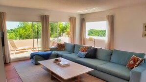 Ein modernes Wohnzimmer mit einem hellblauen Sofa, einem Holztisch und einer großen Schiebeglastür, die zu einem Außenbereich führt.