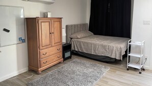 Ein Schlafzimmer mit Bett, Kleiderschrank, Nachttisch, Lampe und Klimaanlage.
