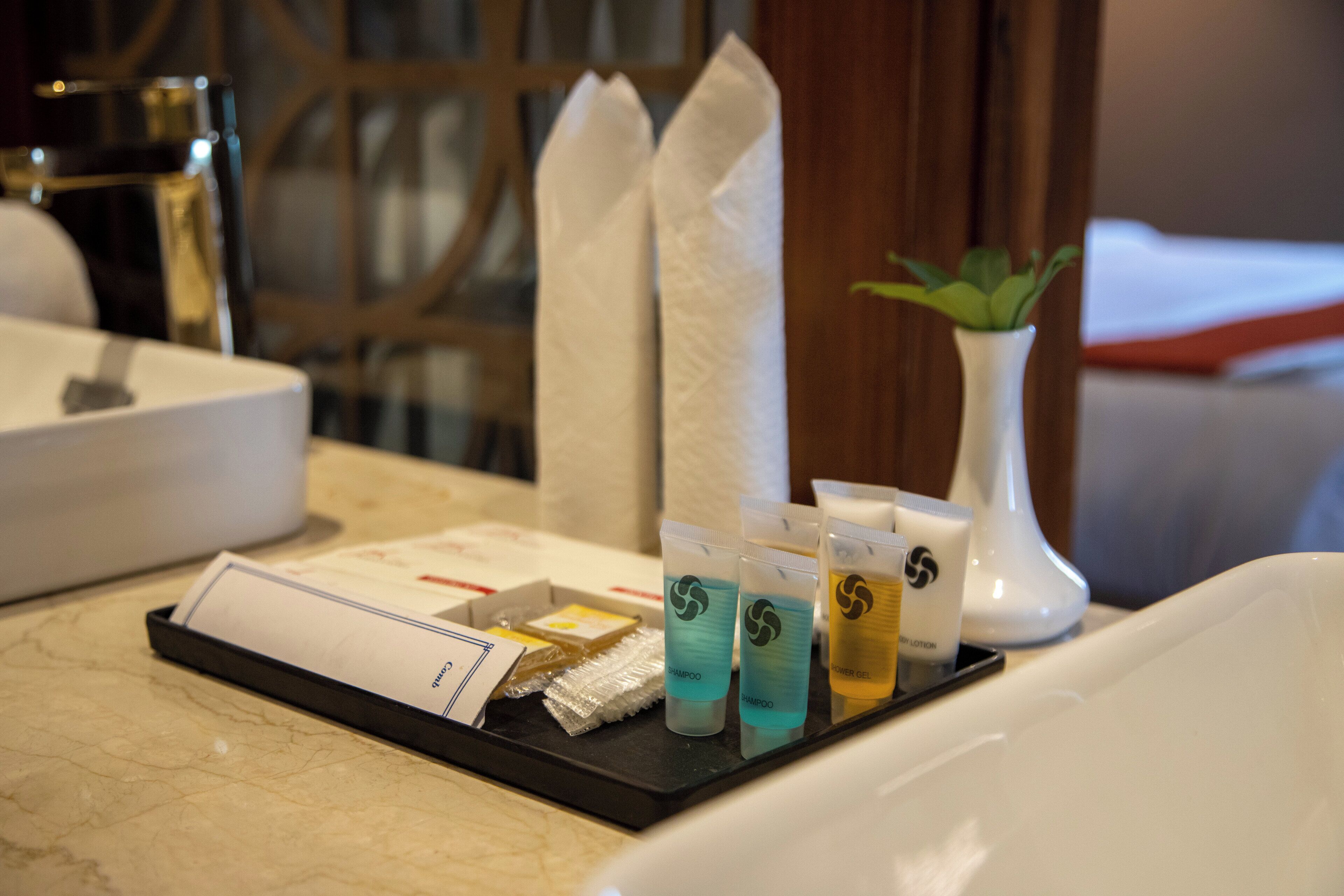 A tray with toiletries including shampoo, lotion, and a tissue box in a hotel room.
