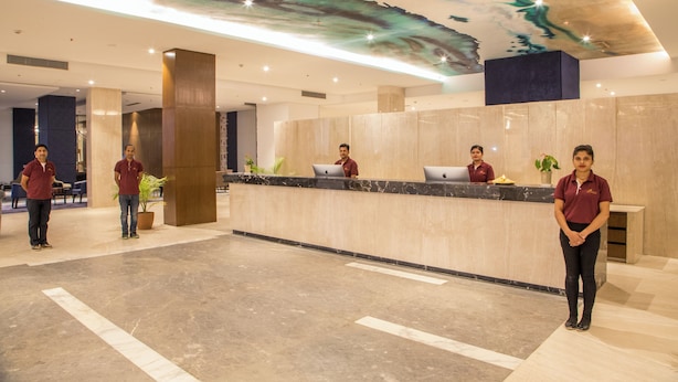 A hotel reception area with a marble counter, staff in uniform, and a ceiling with a natural design.