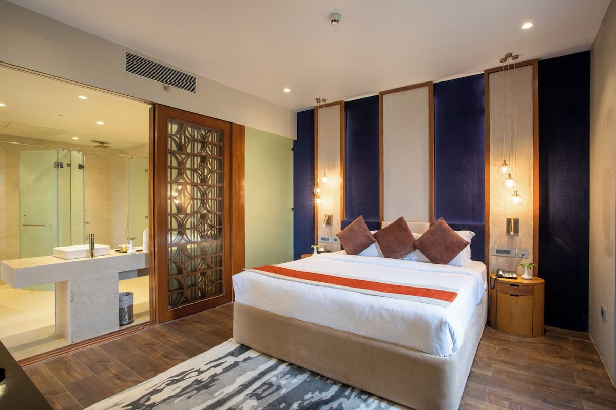 A modern hotel room with a large bed, a bathroom with a vanity, and a decorative screen.