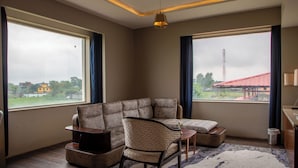A modern living room with a sectional sofa, a small chair, a TV stand, and a view of a residential area through large windows.