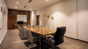 A conference room with a long table, chairs, a projector screen, and a wooden panel wall.