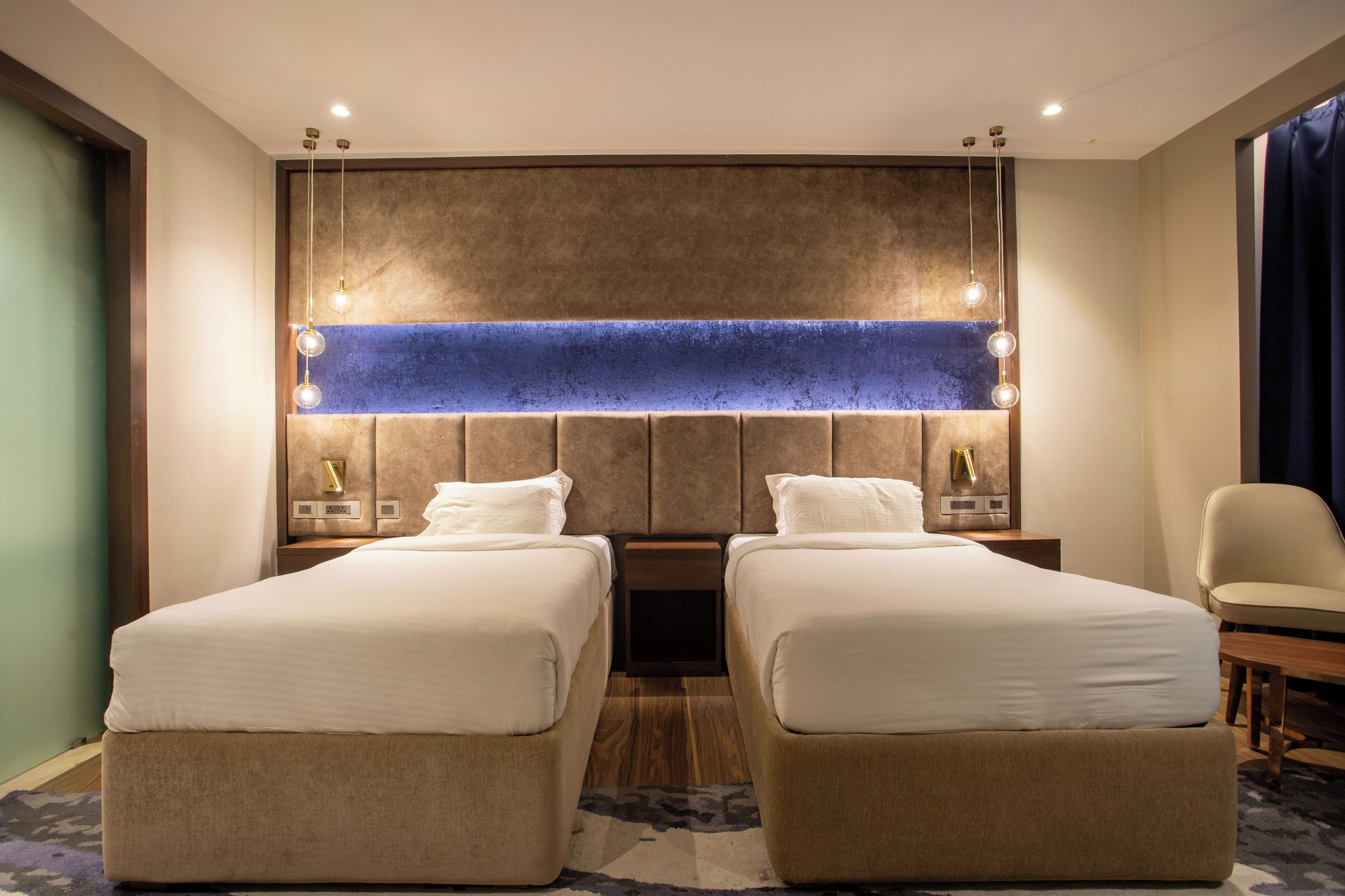 A hotel room with two beds, a large wall-mounted light fixture, a chair, and a small table.