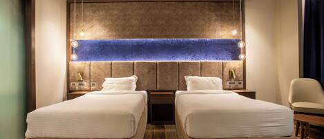 A hotel room with two beds, a large wall-mounted light fixture, a chair, and a small table.