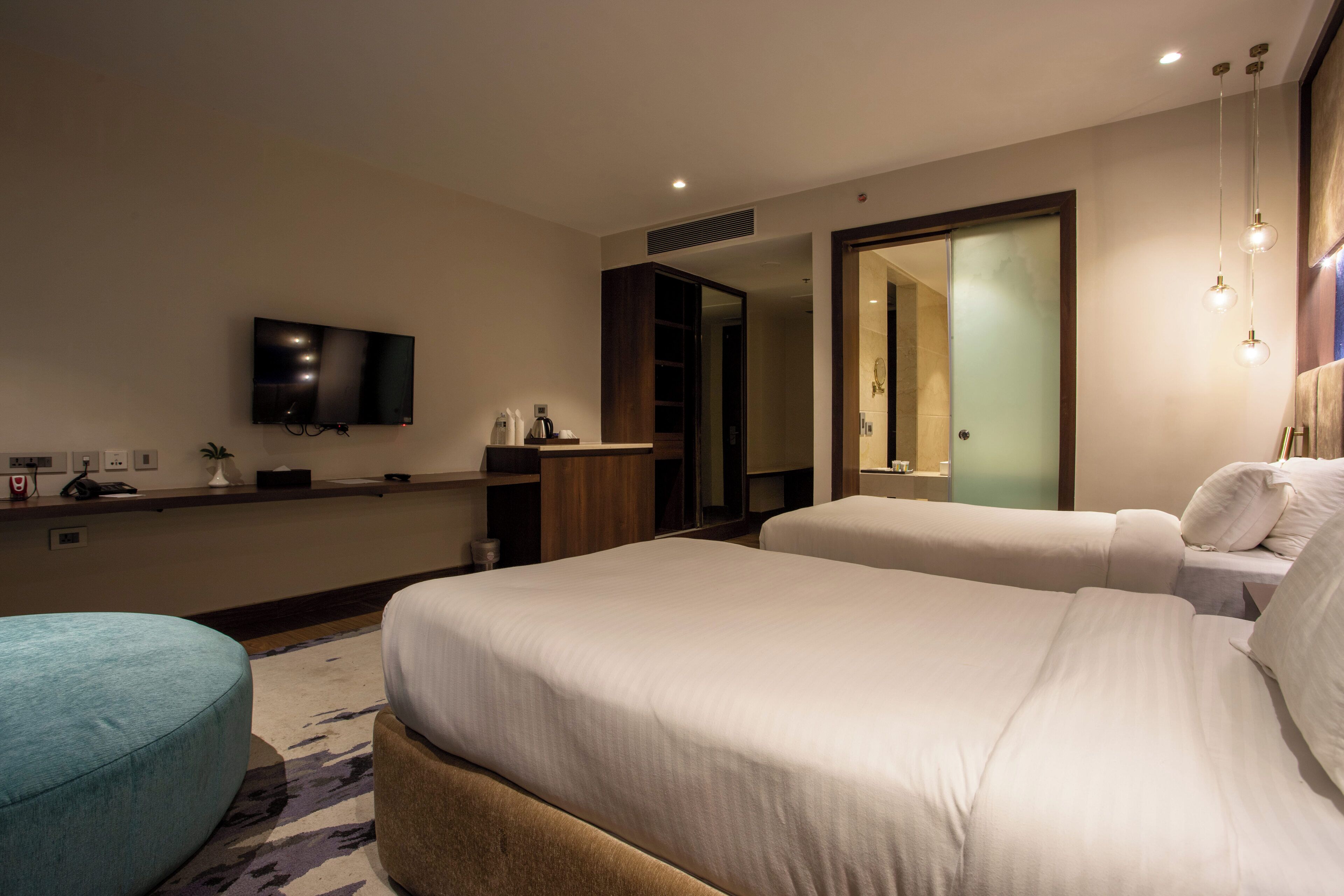A hotel room with a large bed, a small sofa, a TV mounted on the wall, and a mirror.