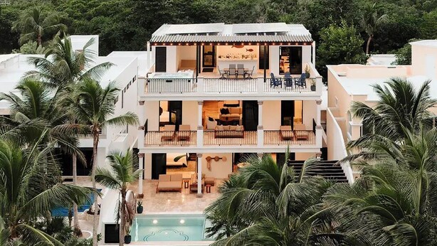Uma casa de dois andares com varanda, piscina e palmeiras.