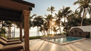 Área de piscina com vista para o mar, palmeiras e um espaço de estar coberto.