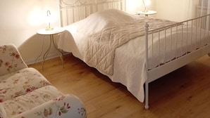 Une chambre à coucher avec un lit en métal, une table de chevet avec une lampe, un canapé à motifs floraux et une lampe fixée au mur.