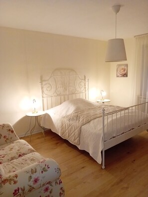Un dormitorio con estructura metálica para la cama, una mesita de noche con lámpara, un sofá floral y una lámpara de pared.