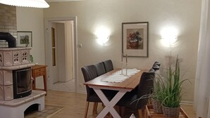 Un coin repas avec une table en bois, des chaises et un canapé. On y trouve également une cheminée, un luminaire fixé au mur et un tableau encadré accroché au mur.