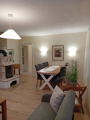 Un comedor con una mesa de madera, sillas y un sofá. Hay una chimenea, una lámpara de pared y un cuadro en la pared.