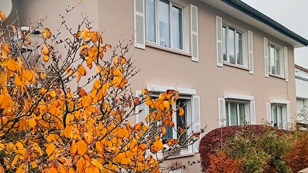Un immeuble résidentiel de deux étages, doté d’un toit plat, de volets blancs et d’un chemin en briques menant à l’entrée.