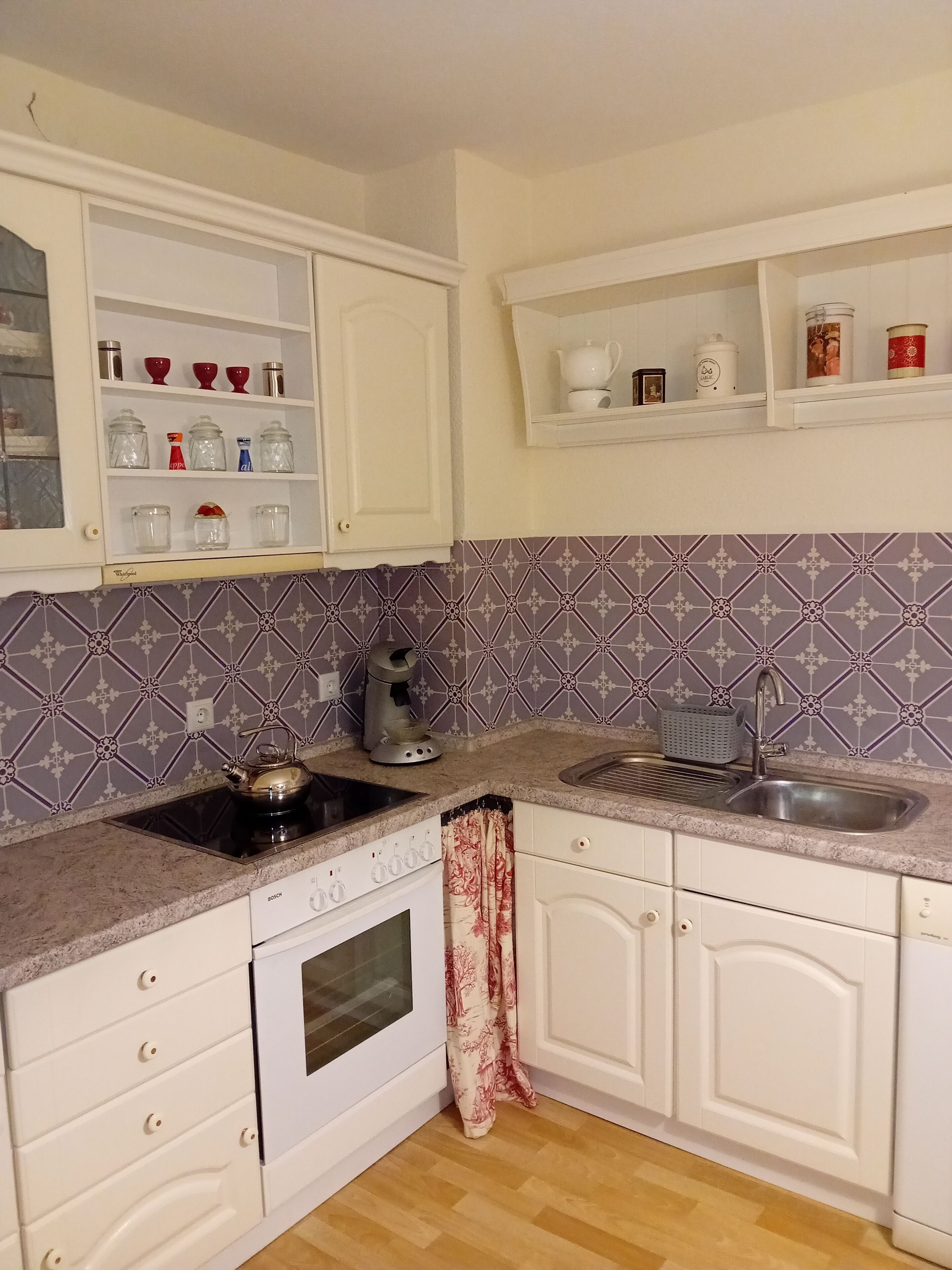 Een keuken met witte kastjes, een Bosch vaatwasser, een waterkoker en een spoelbak.