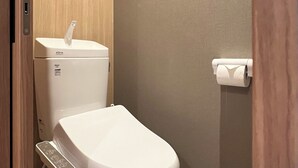 Een badkamer met een toilet, een papieren handdoekdispenser aan de muur en een houten paneel boven het toilet.