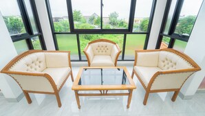 Una habitación con una mesa de centro de vidrio y dos sillones tapizados con estructura de madera, ubicados frente a amplios ventanales con vistas a zonas verdes y edificios.