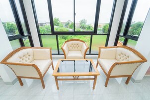 Una habitación con una mesa de centro de vidrio y dos sillones tapizados con estructura de madera, ubicados frente a amplios ventanales con vistas a zonas verdes y edificios.