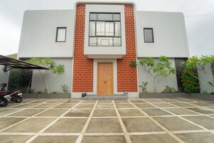 Un edificio moderno con un área de entrada con baldosas, una puerta central y dos ventanas.