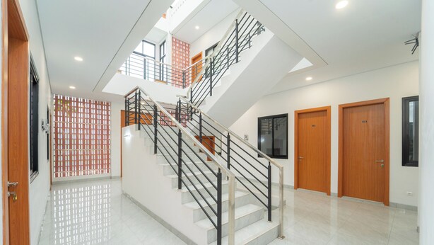Un interior moderno con una escalera central, puertas de madera y piso de baldosas.