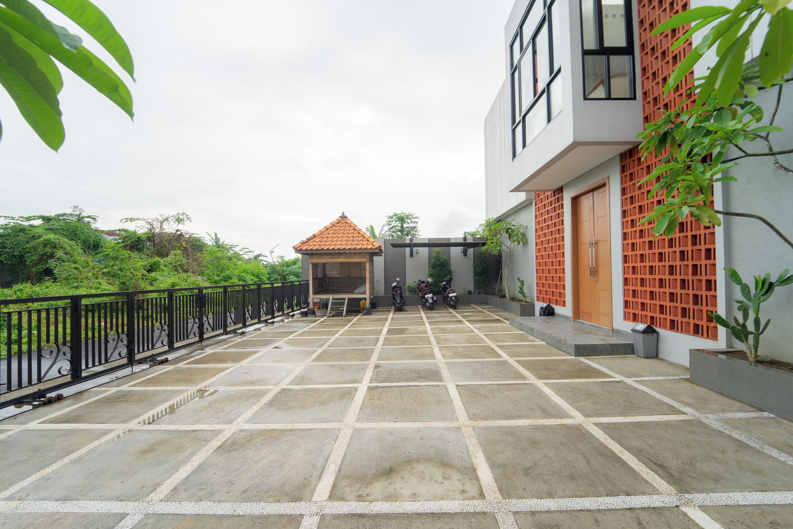 A courtyard with a tiled floor, a small building with a tiled roof, and a modern building with a red lattice facade.