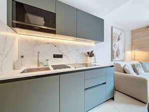 Una cocina moderna con microondas integrado, un lavamanos y una estufa. Hay un comedor con un sofá y un cuadro en la pared.