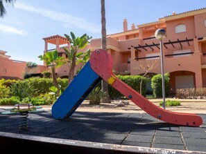 A playground with a slide and swings in front of a building with a tiled roof and balconies. - Private garden | Beach 8 min | Netflix | Desk (Vera)