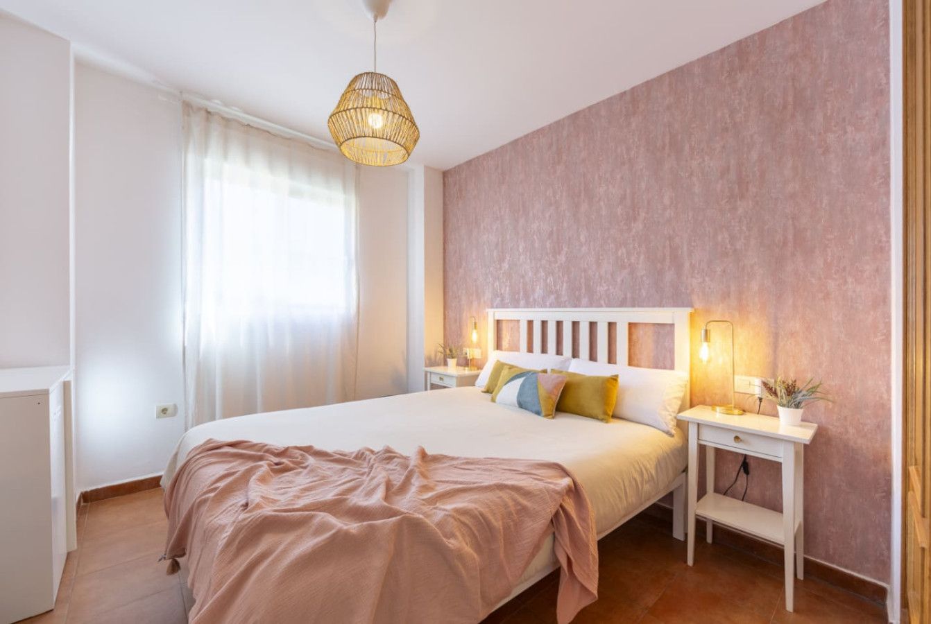 Un dormitorio con una cama grande, mesitas de noche, una lámpara colgante y una ventana con cortinas.