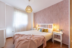Een slaapkamer met een groot bed, nachtkastjes, een hanglamp en een raam met gordijnen.